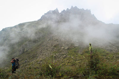 Side view of backpacker standing on mountain during foggy weather