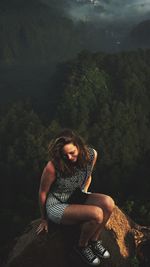 Portrait of woman sitting on rock against trees