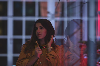 Young woman looking away while standing against glass window