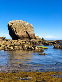 Rock formation in sea against clear blue sky