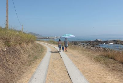 Rear view of people walking on road along calm sea