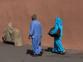 Rear view of people walking in street against wall