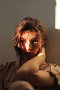 Close-up portrait of woman sitting against wall at home