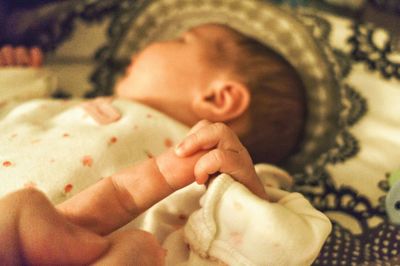 Baby sleeping while holding father finger at home