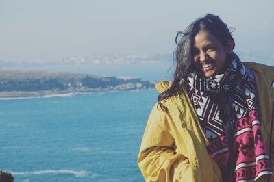 Portrait of young woman standing by sea against sky