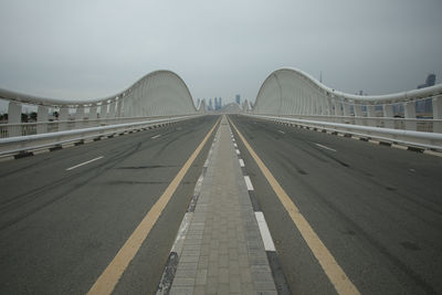 Road leading towards bridge against sky in city