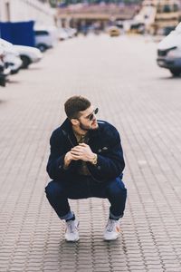 Full length of man sitting on footpath in city