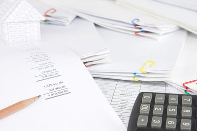 High angle view of calculator and pencil with model house on financial documents