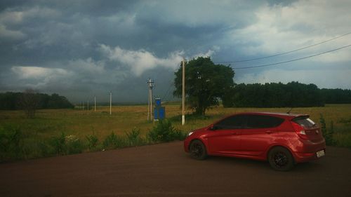 Road passing through field against cloudy sky