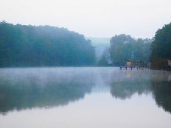 Reflection of trees in calm lake against sky during foggy weather