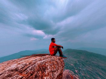 Man on rock by sea against sky