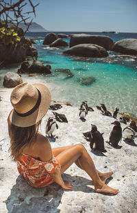 Woman in hat sitting by penguins at beach