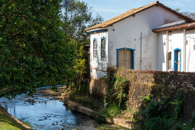 Houses by river amidst trees and buildings against sky