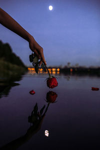 Close-up of hand with fruits on lake against sky at dusk