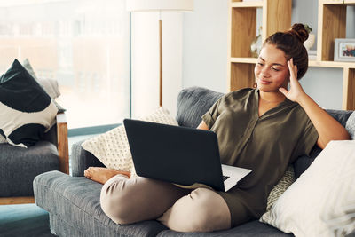 Young woman using mobile phone while sitting on sofa at home