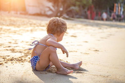 Side view of shirtless boy sitting on sand at beach