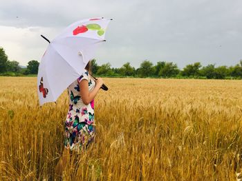 Back of woman holding an open umbrella in a field of ripe wheat