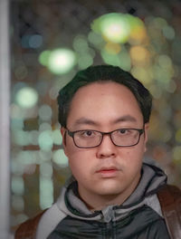 Close-up portrait of young man wearing eyeglasses against street and neon lights at night.