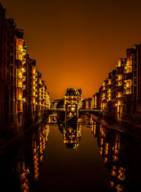 Illuminated buildings by river against sky at night