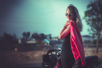Portrait of smiling woman wearing sunglasses standing by motorcycle