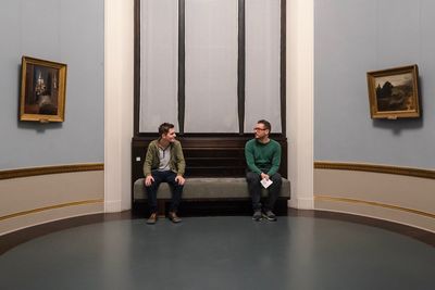 Full length of friends talking while sitting on sofa in museum