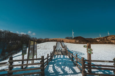 Snow covered footbridge against blue sky