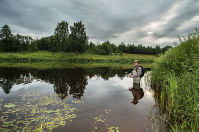 Mature man fishing at lake against sky