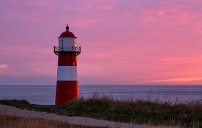 Lighthouse by sea against sky during sunset