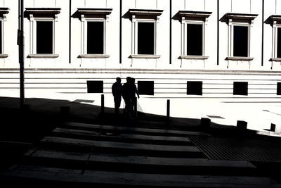 Silhouette men on footpath against building