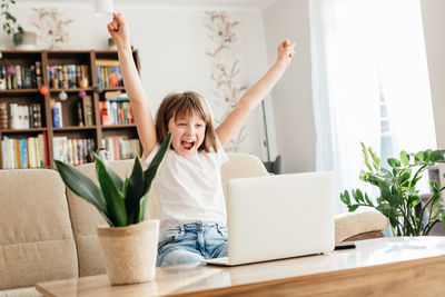 Girl schoolgirl at home in front of a laptop rejoices at success. online learning