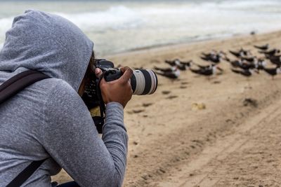Side view of woman photographing birds at beach