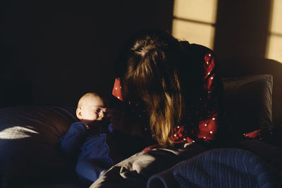 Mother sitting with baby on bed at home