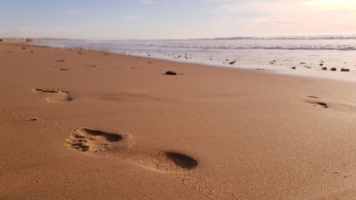 Footprints on sand at beach against sky