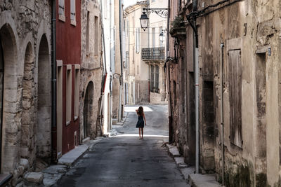 Rear view of girl walking on alley amidst old buildings in town