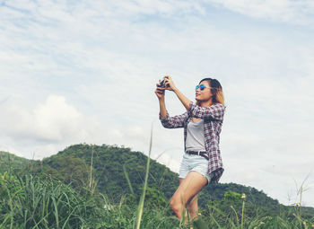 Woman photographing while standing on field against sky