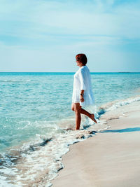 Young woman in cover up plays with sea waves on the beach