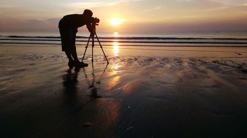 Silhouette man photographing at beach during sunset