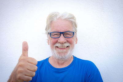 Portrait of smiling senior man gesturing against wall