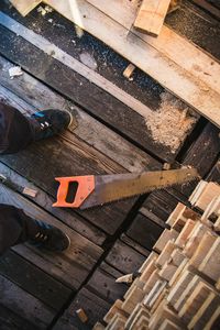 Low angle view of man standing by hand saw by planks on floorboard