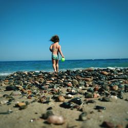 Pebbles at beach with girl walking against blue sky in background