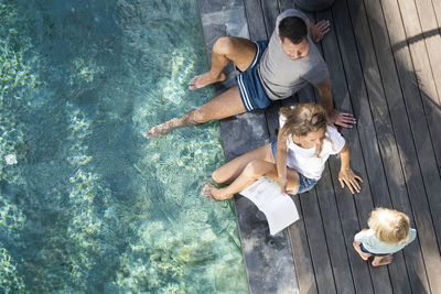 Family sitting at the swimming pool, mother reading book for children