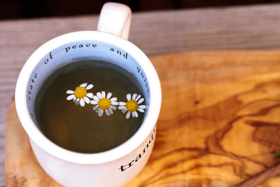 High angle view of chamomile tea with daisies in cup on cutting board