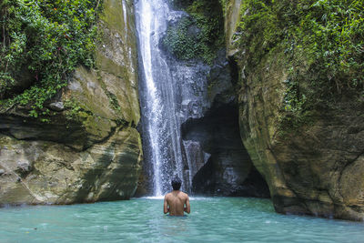 Shirtless man standing against waterfall