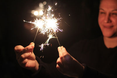 Midsection of woman holding sparkler at night