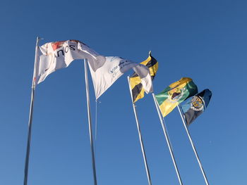 Low angle view of flags against clear blue sky