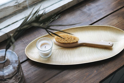 Details of interior, aromatic candle in glass and wooden brush with natural bristles on metal tray 