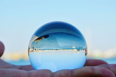 Close-up of hand holding crystal ball against sea