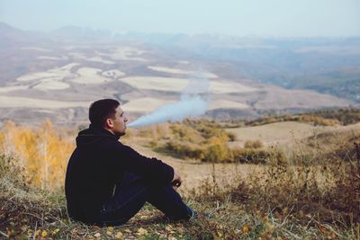 Man sitting on field against mountain