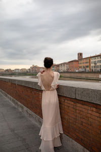 Rear view of woman standing by retaining wall against city