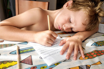 Shirtless boy writing in book at home